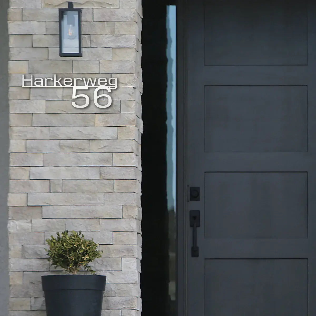 Ein Edelstahlschild mit dem Straßennamen und Hausnummer hängt neben einer grauen Haustür an der Wand