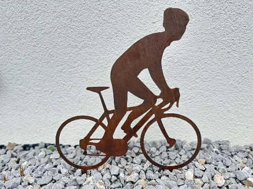 Gartenstecker mit dem Motiv eines Radfahrers in Cortenstahl gerostet in einem Steinbeet vor einer weißen Hauswand